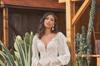 Chica morena con la melena suelta con un vestido de novia de corte sirena con manga larga con transparencias