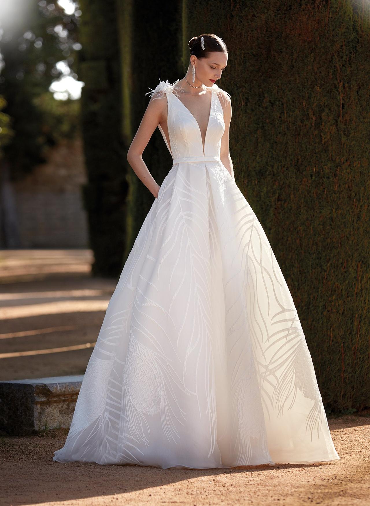 Chica con el pelo recogido con un vestido de novia con profundo escote en V y plumas en los hombros