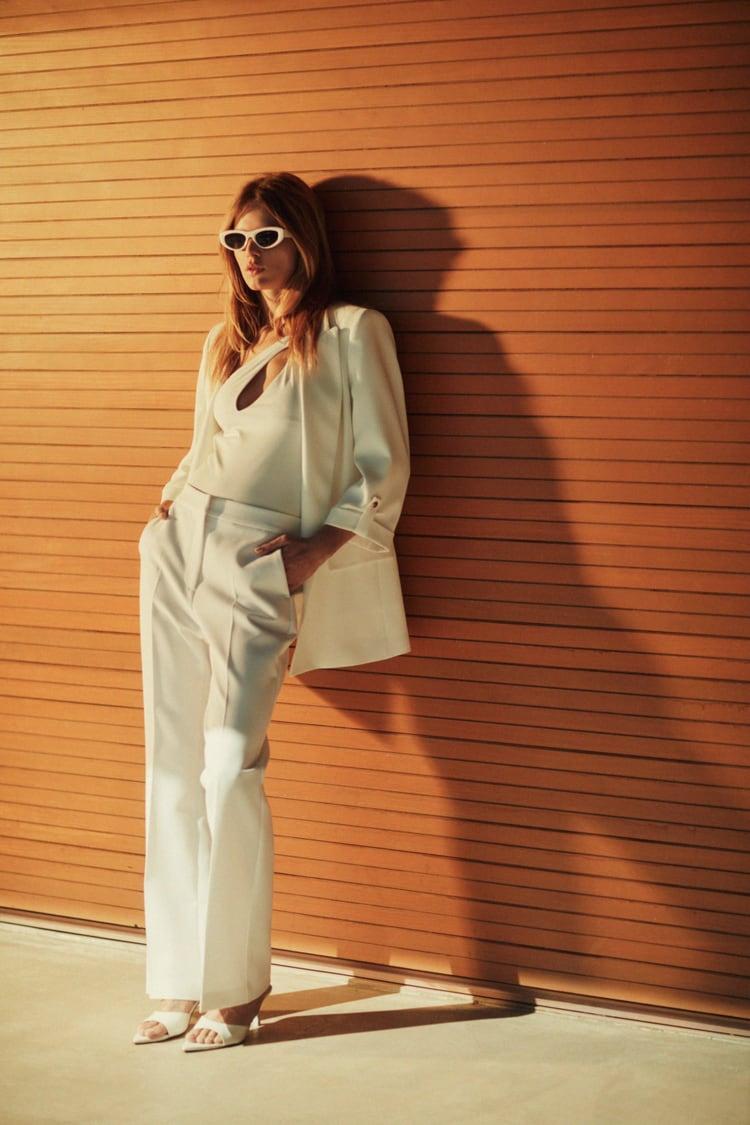 modelo con raje de chaqueta y pantalón blanco, top asimétrico y gafas de sol blancas de estilo retro