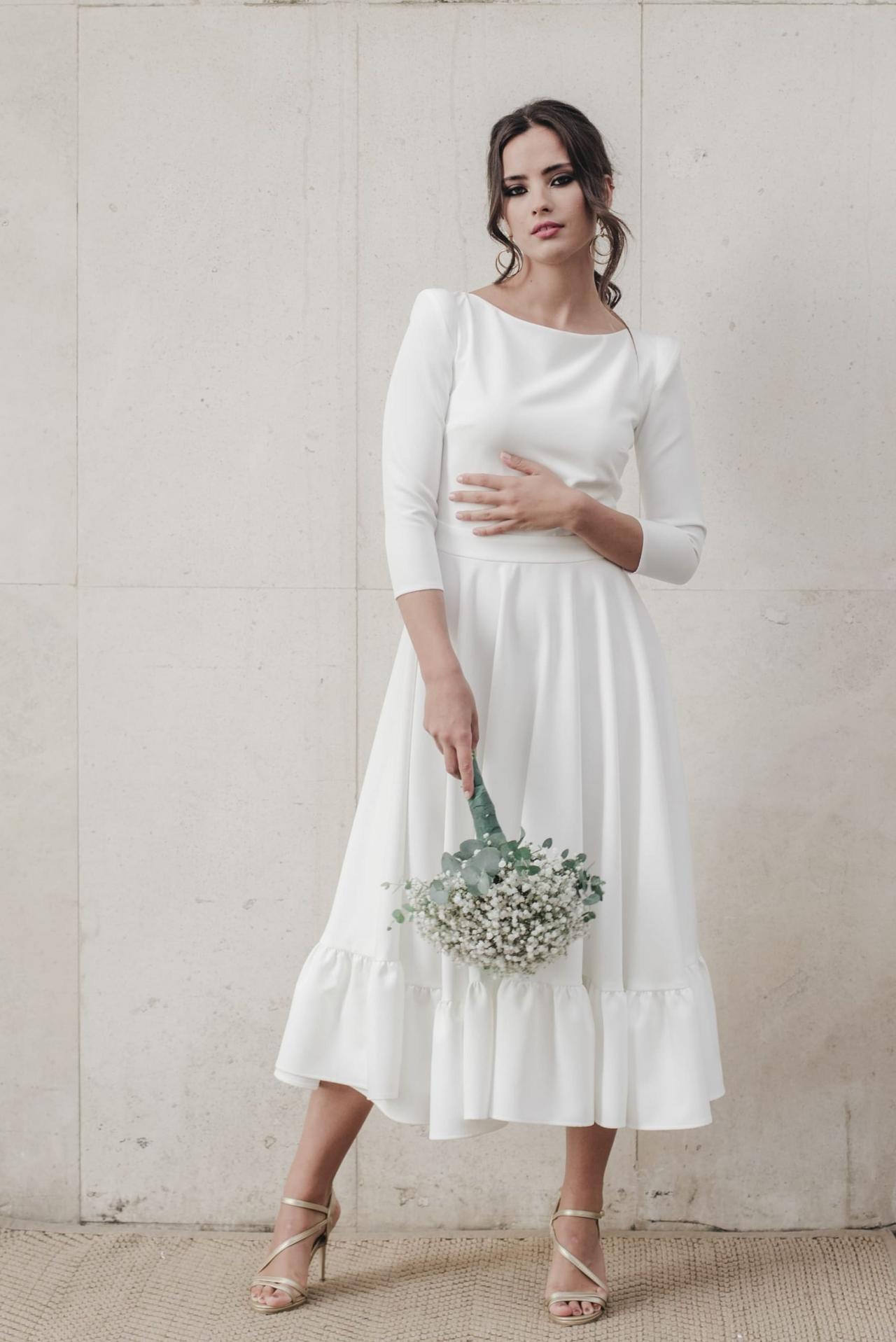 Chica morena con el pelo recogido con un vestido blanco de largo midi con manga francesa y volante en el bajo de la falda