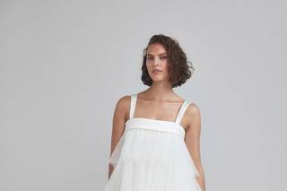 Chica con media melena rizada suelta con un vestido blanco de largo midi con volantes de estética años 20
