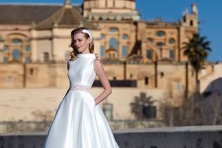 Vestido de novia de corte princesa, sin mangas, con detalle decorativo en la cintura y cuello cisne