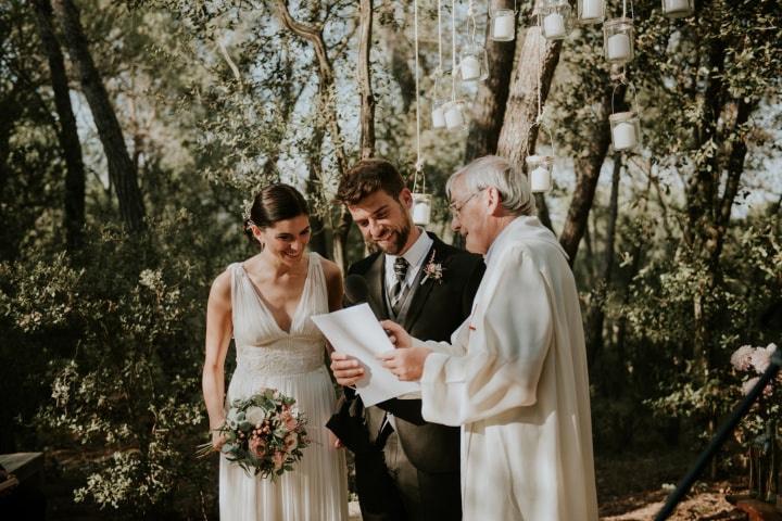 Boda religiosa fuera de la iglesia: sacerdote comentando algo a una pareja casadera en un precioso jardín decorado para la boda