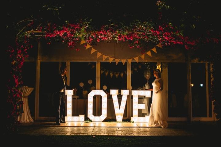 Pareja el día de la boda junto a unas letras luminosas con la palabra Love