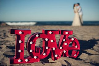 Letras metálicas de color rojo en las que puede leerse la palabra Love sobre la arena de la playa el día de la boda