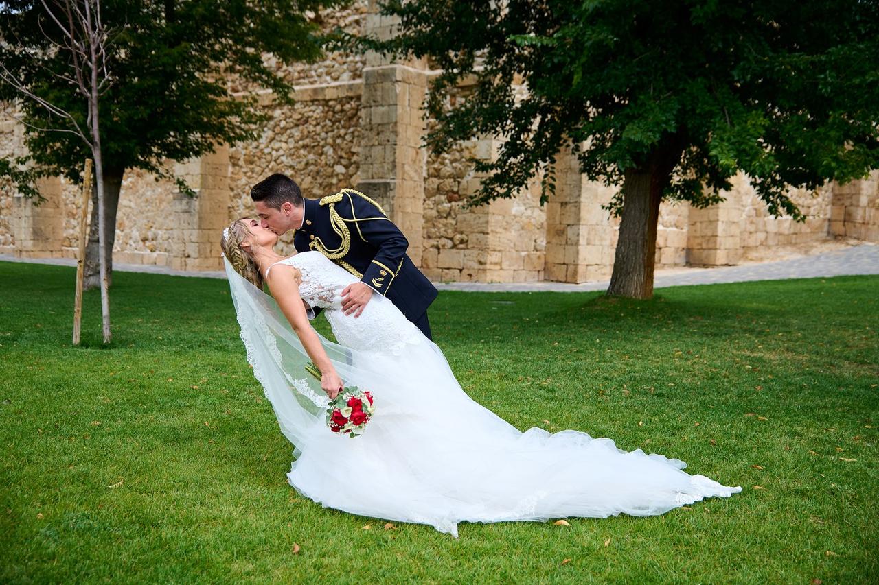 Pareja de recién casados se besa en un exterior: ella con un vestido de novia y él con traje de militar