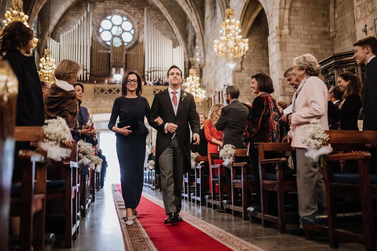 Madrina boda caminando por el pasillo de una iglesia hacia el altar del brazo del novio