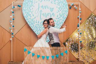 Pareja de recién casados en divertida pose delante de un corazón con fondo azul y sus nombres en su photocall boda