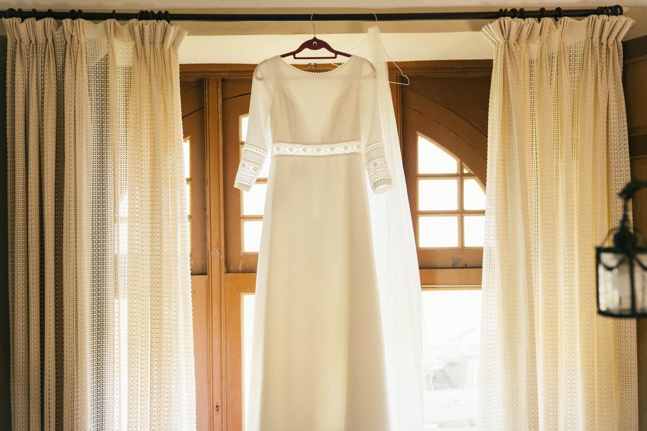 Vestido de novia de manga larga y cuello redondo colgando de la barra de las cortinas de una habitación