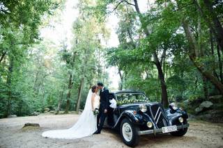 Coche clásico decorado con flores con una pareja vestida de novios apoyada en él