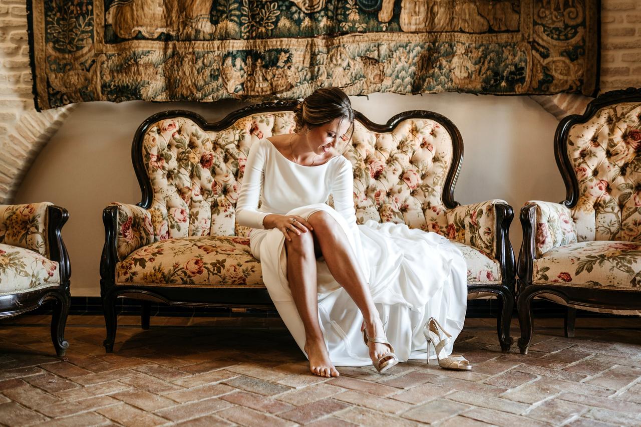 Algo nuevo, algo viejo, algo prestado: chica vestida de novia muy sonriente poniéndose unos zapatos de tacón alto