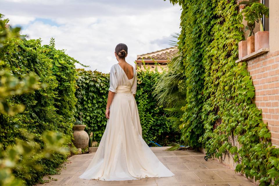 Novia de espaldas con el pelo recogido y un precioso vestido con manga francesa, escote en la espalda y cintura definida