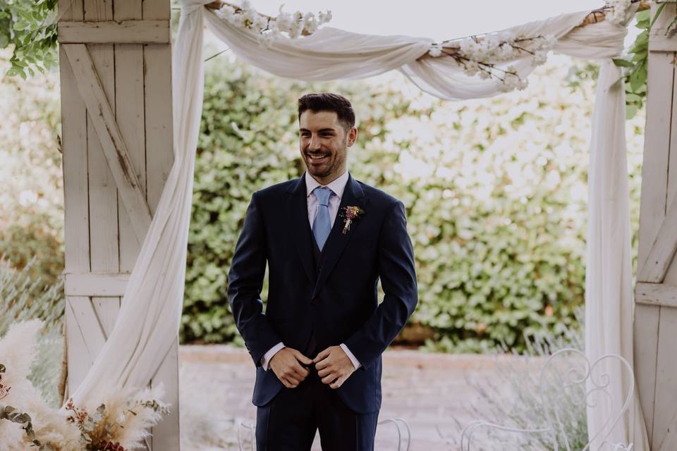 Novio con traje y corbata en color azul esperando a su pareja en el altar de una ceremonia civil al aire libre