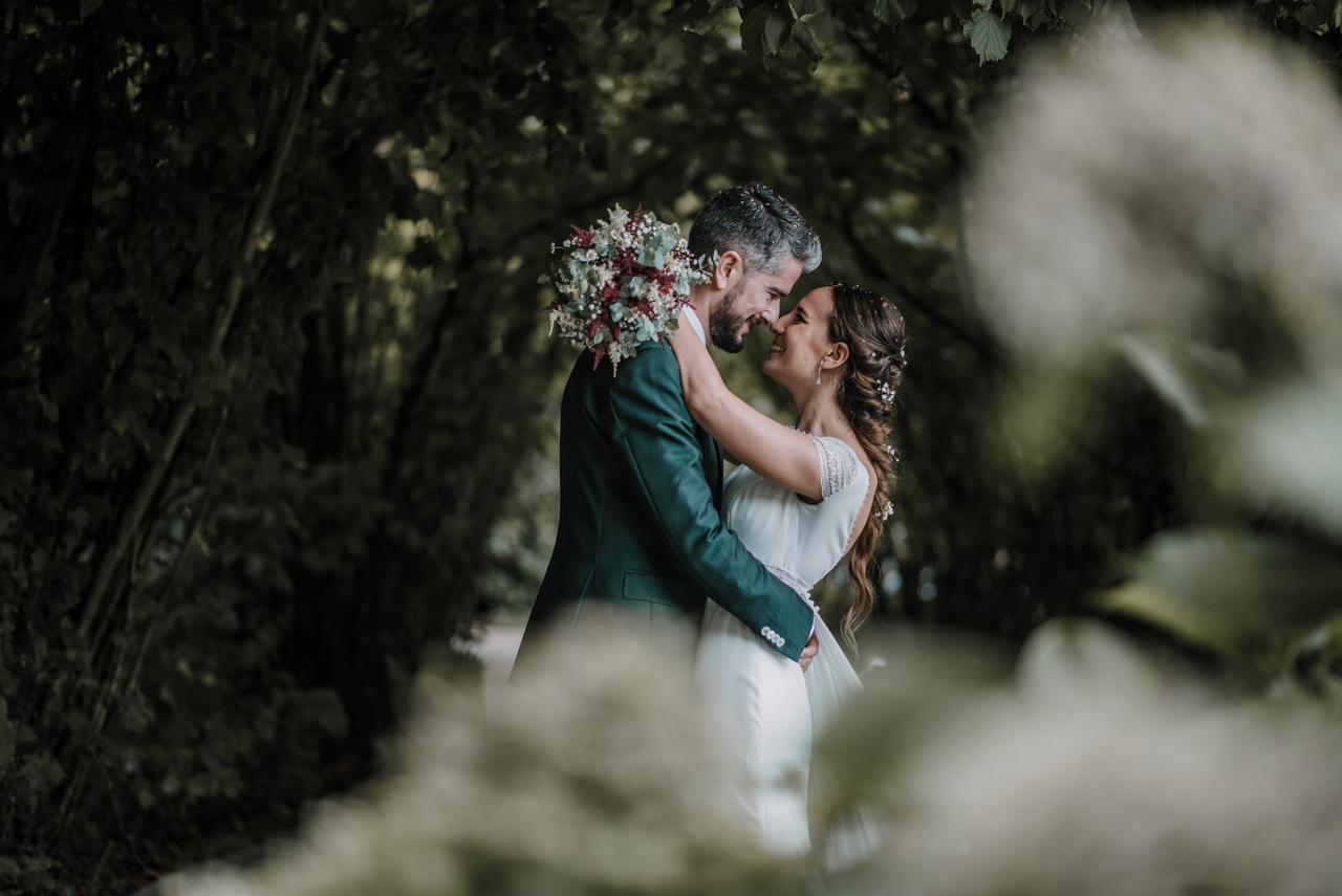 Checklist boda: chico y chica vestidos de novios se abrazan muy sonrientes y rodeados de árboles