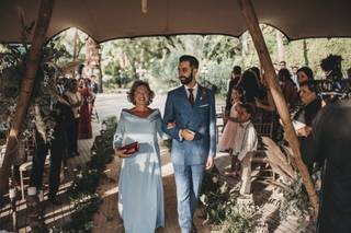 Madrinas de boda: novio con traje y madrina con gafas y un precioso vestido azul cielo caminan del brazo hacia el altar de su boda civil al aire libre