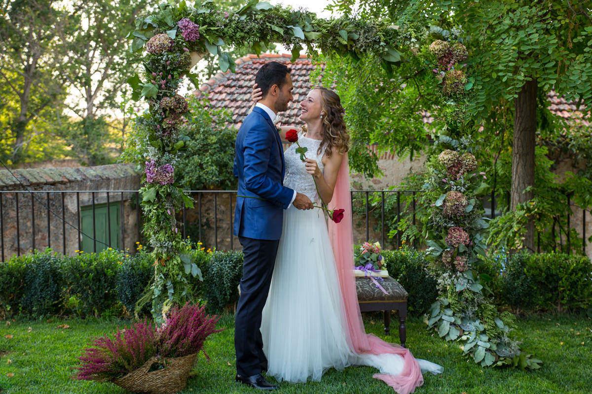 Chico y chica vestida de novia se miran sonrientes a la cara mientras sujetan unas rosas en sus manos
