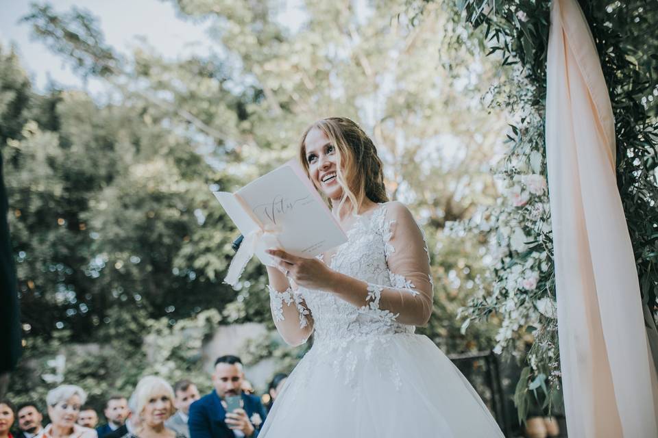 Escribir votos matrimoniales: novia en el altar de una ceremonia civil al aire libre leyendo sus votos matrimoniales a su pareja