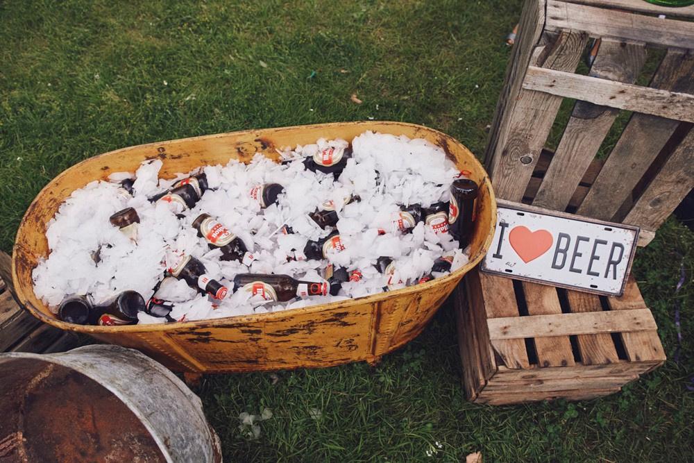 Rincón cerveza boda con recipiente de forma rectangular sobre el césped y lleno de hielo y de cervezas