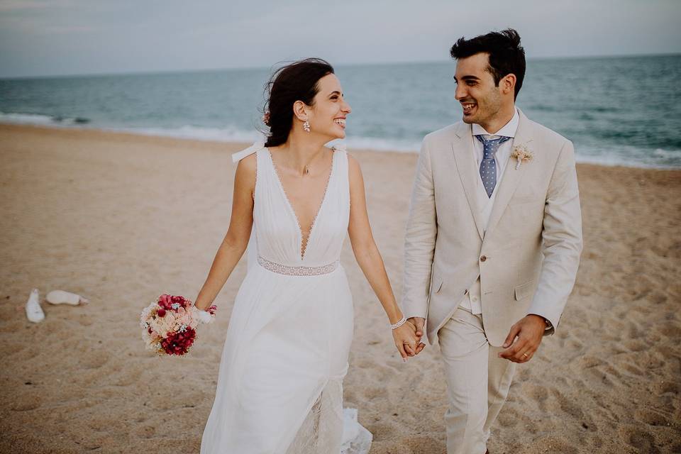 Pareja feliz paseando por la playa durante la sesión fotográfica el día de su boda en verano