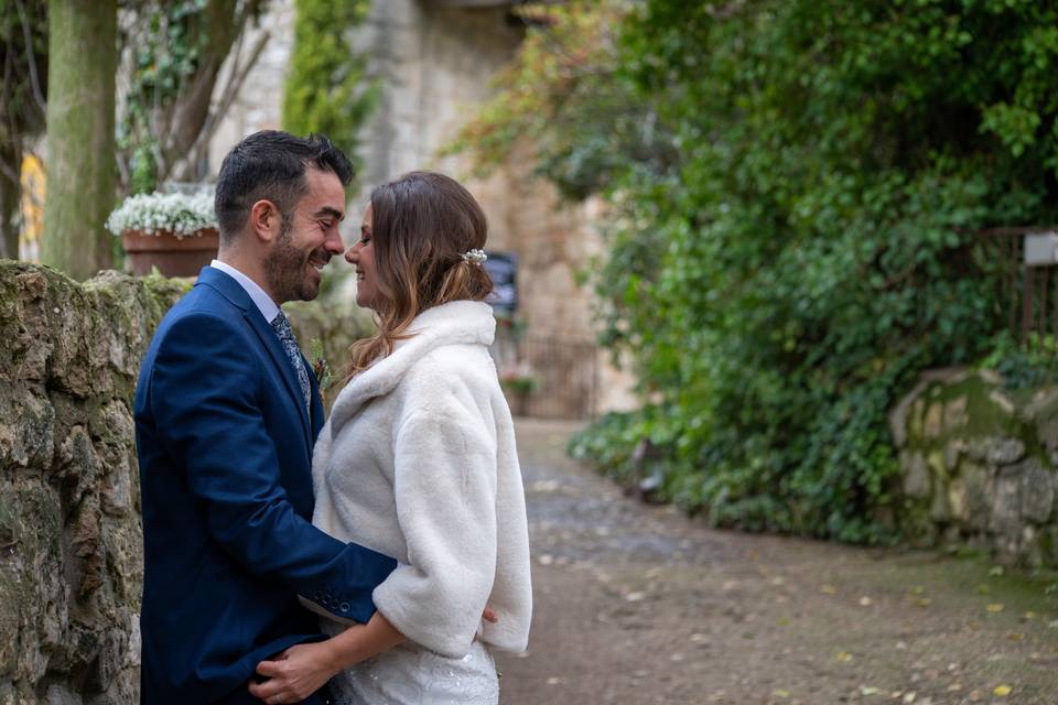 Chico con traje azul y chica con chaqueta blanca se abrazan acaramelados en un bonito exterior