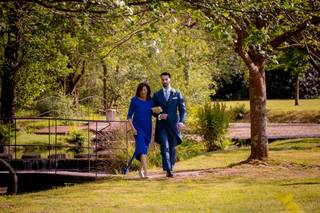 Madrinas de boda: novio con traje y madrina con vestido azul de largo midi caminan cogidos del brazo por un ambiente al aire libre