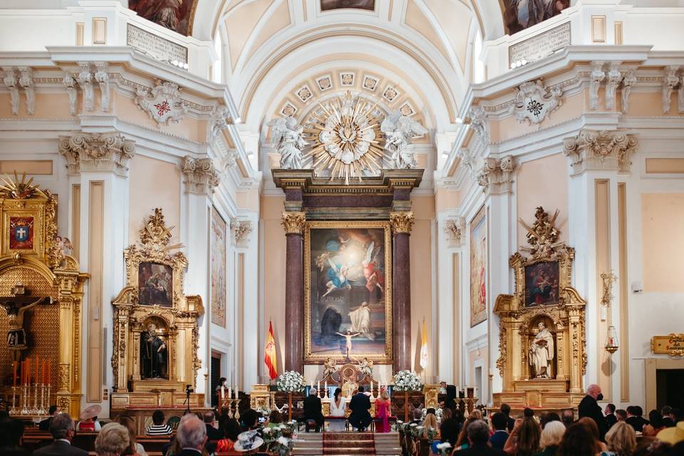 Interior de una iglesia de gran tamaño con los novios y los padrinos sentados en el altar