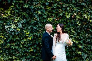 Chica vestida de novia con su larga melena morena suelta y chico con traje oscuro se cogen de la mano muy sonrientes