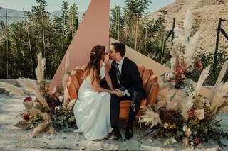 Novia con pelo suelto besando a su pareja sentada en el sofá de su altar de boda civil al aire libre