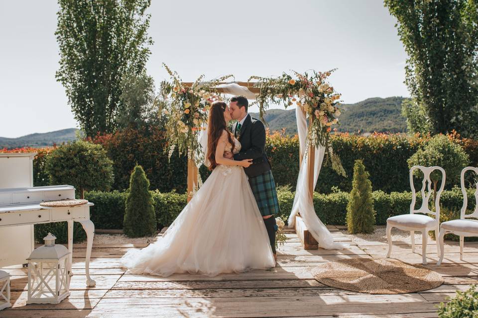 Boda celta: pareja en el altar de su boda civil al aire libre besándose, él con falda escocesa