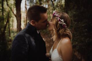 Pareja de chico y chica, ella con corona de flores naturales, dándose un beso en medio del bosque