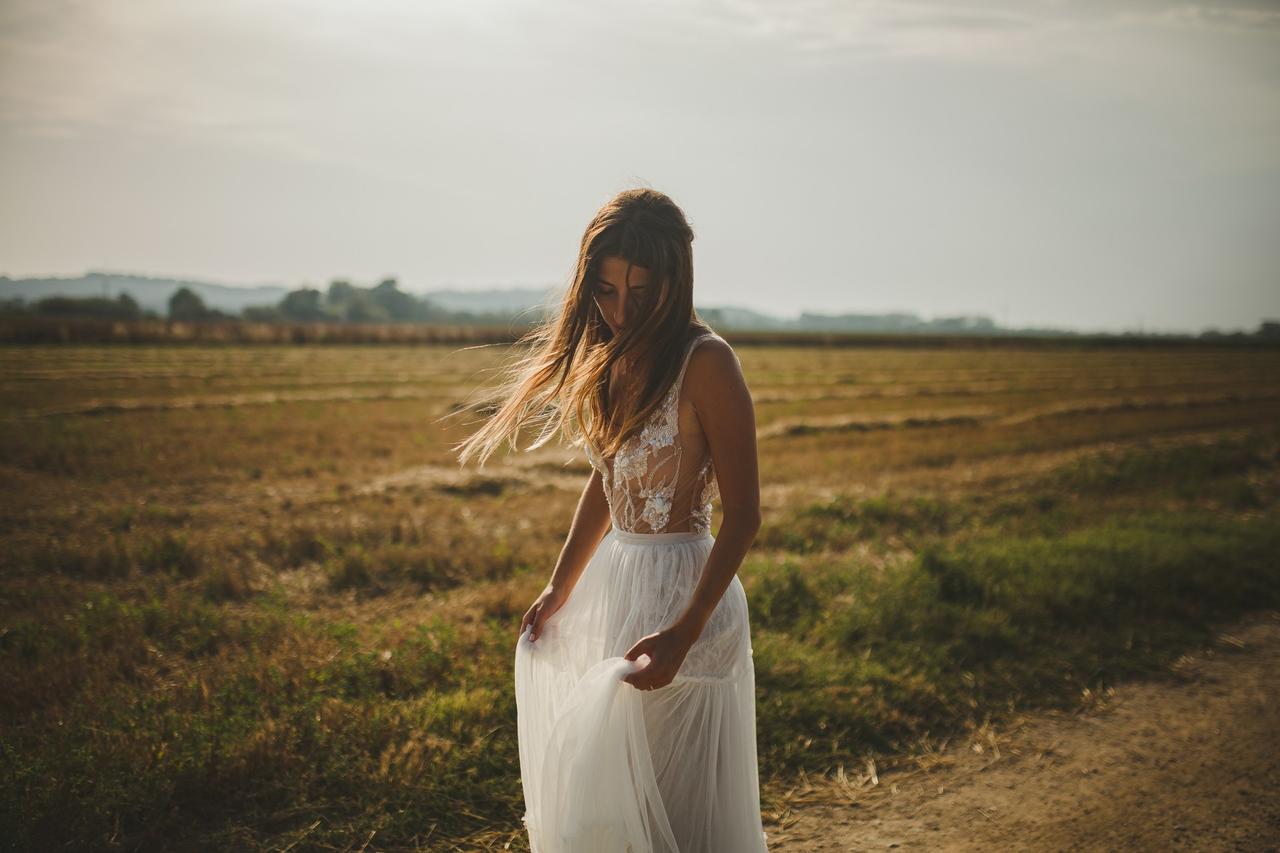 Novia se sujeta la falda en un exterior mientras el viento despeina suavemente su melena suelta