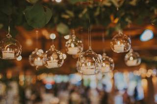 Decorativas piezas de cristal transparente con velas en su interior colgando de las ramas de un árbol