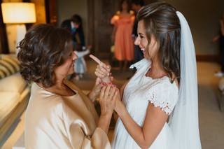 Madrinas de boda: novia muy sonriente coge las manos de su madre y madrina