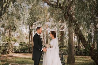 Chico con traje y chica vestida de novia se cogen las manos mientras se miran fijamente a los ojos en un precioso jardín con mucha vegetación