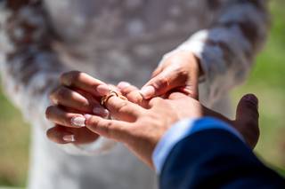 Dónde se pone el anillo de casado: mano femenina le pone el anillo de casado a una mano de hombre en una ceremonia civil al aire libre