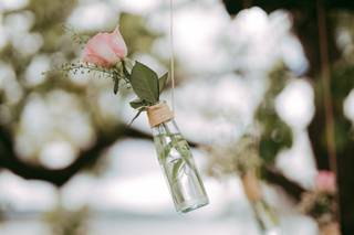 Decoración boda exterior: botellas de cristal transparente suspendidas con una rosa de color rosa en su interior