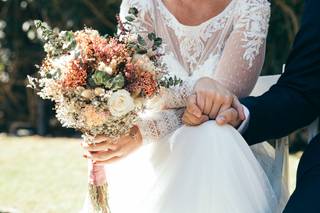 Novia y novio sentados en el altar y cogidos de una mano mientras ella sujeta con la otra su bonito ramo de flores