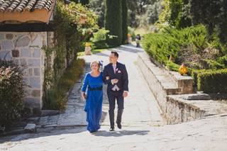 Madrinas de boda: novio con traje y madrina con un precioso vestido azul klein caminan del brazo por un camino