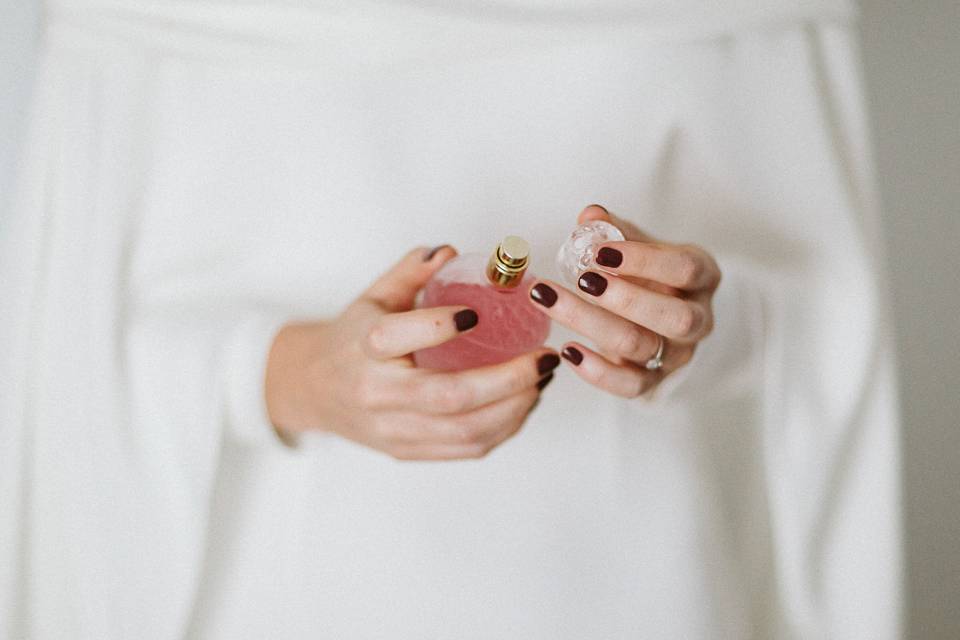 Chica vestida de blanco y con las uñas en un tonalidad morada sostiene una botella de perfume entre sus manos