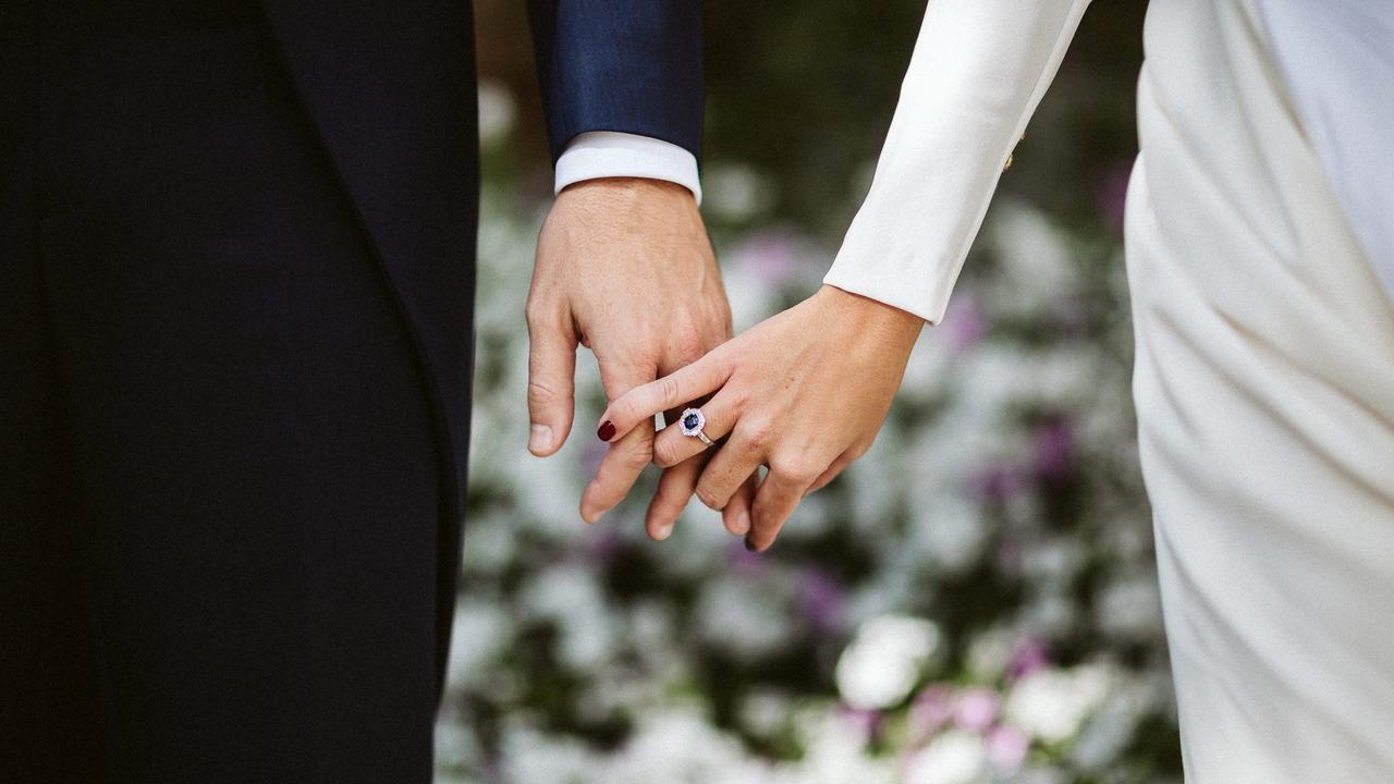 Calculadora Bodas.net: pareja de recién casados se coge de la mano, dejando en primer plano el anillo de pedida de la novia