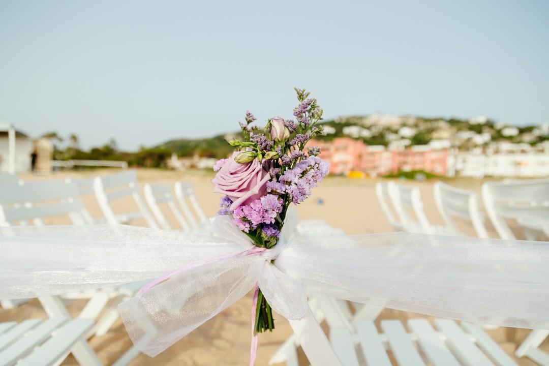 Ramillete de flores decora el respaldo de una silla durante una ceremonia de boda en la playa