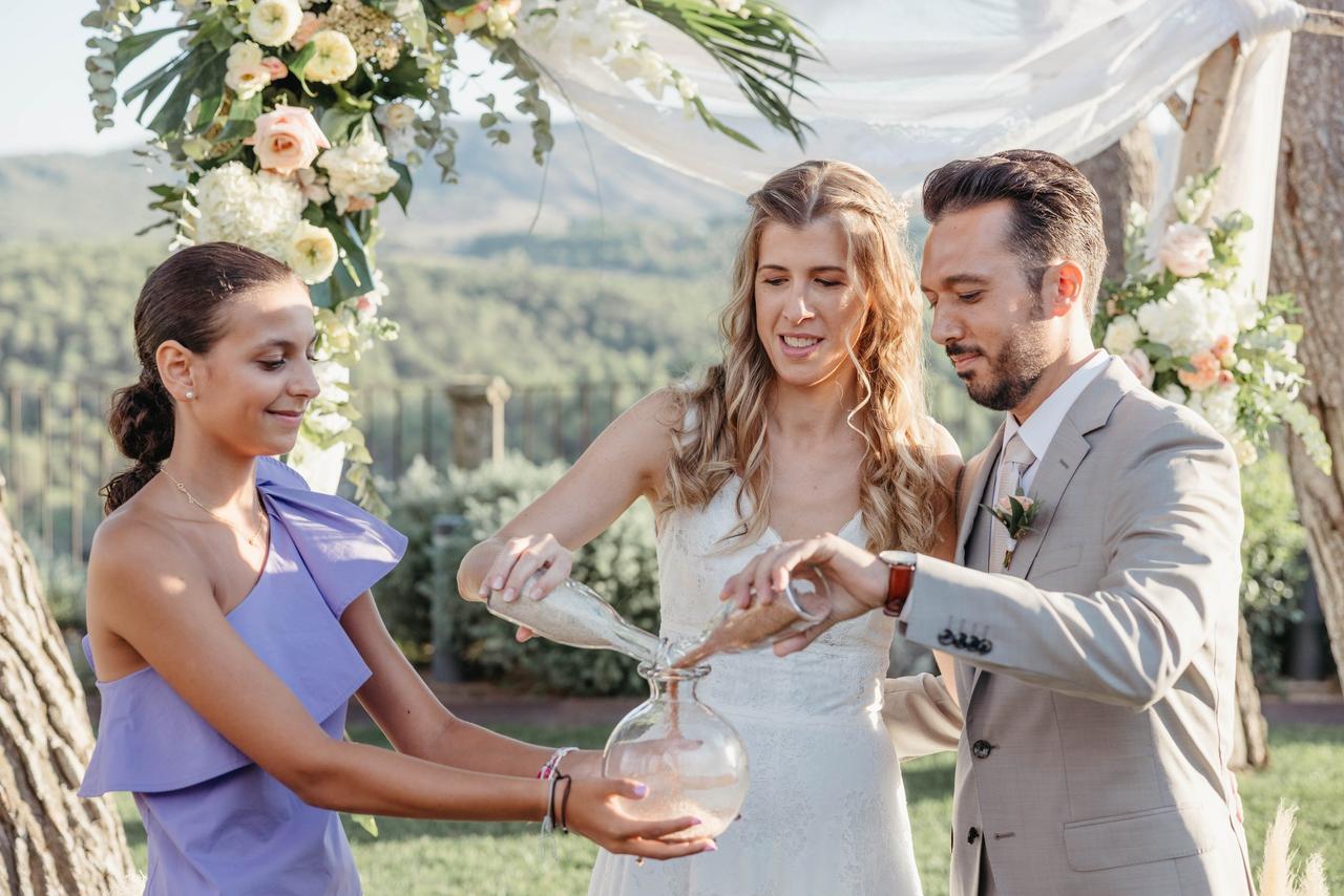 Pareja en el altar de su boda civil al aire libre mientras celebran la ceremonia de la arena con la ayuda de una adolescente