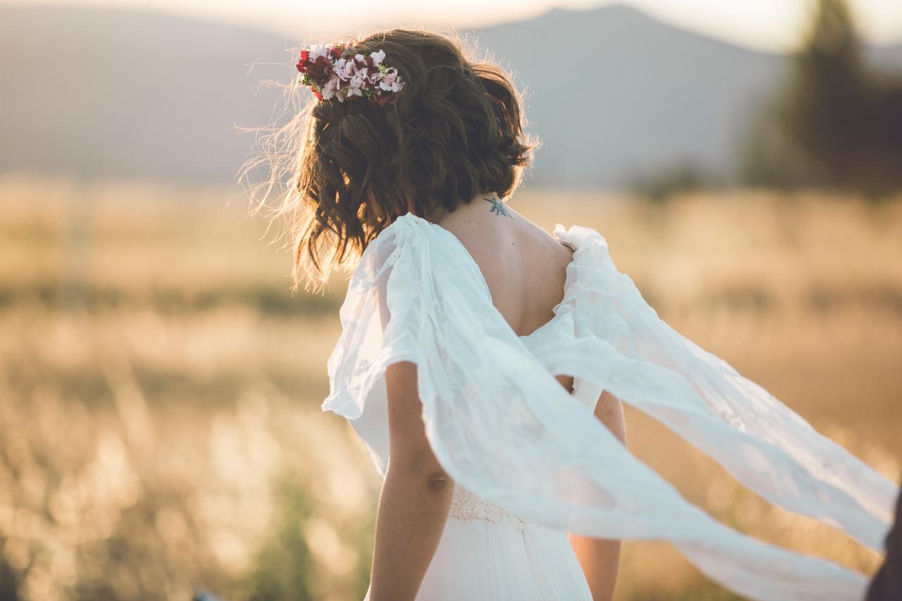 Novia de pelo corto caminando en medio de un campo vestida de novia