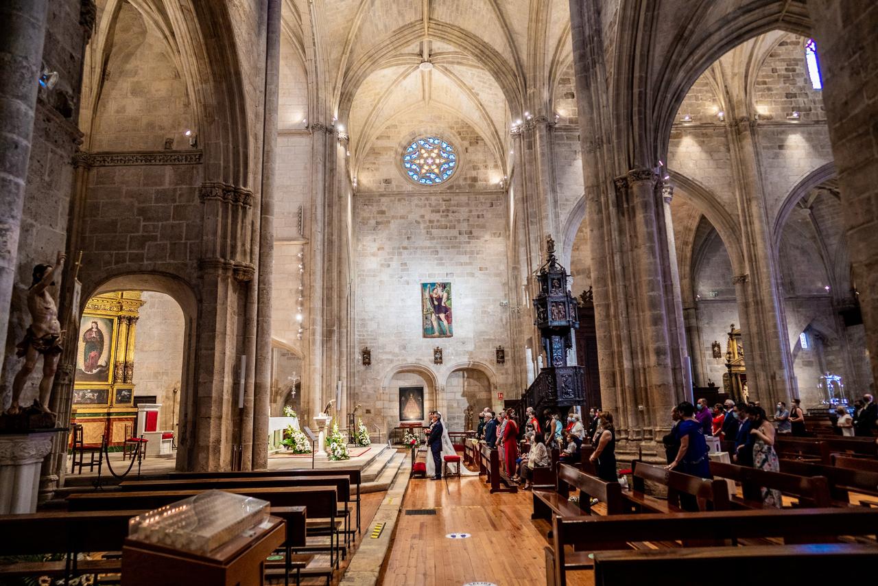 Vista lateral del interior de una iglesia de gran tamaño durante la celebración de una boda religiosa con los novios en el altar