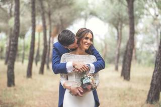 Peinados boda con flequillo: chico con traje abraza a chica vestida de novia en un precioso ambiente al aire libre