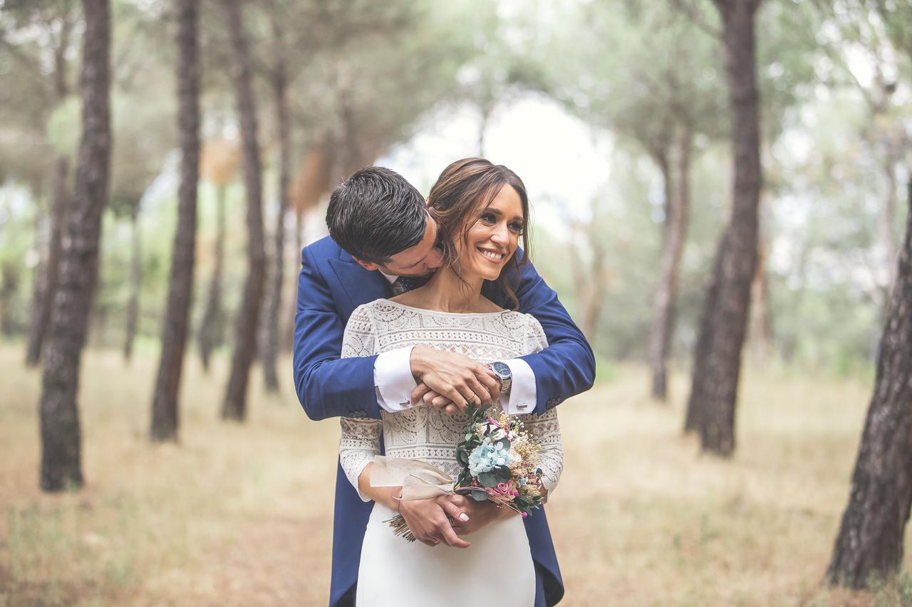 Chico con traje abraza a chica vestida de novia en un precioso ambiente al aire libre