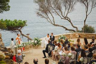 Boda religiosa fuera de la iglesia: sacerdote con un monaguillo al lado oficiando una ceremonia religiosa en un bonito espacio al aire libre 