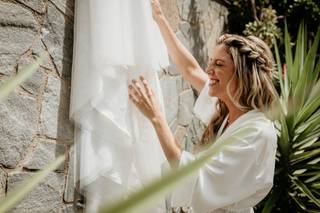 Chica rubia con peinado de novia con trenzas y pelo suelto sonriendo mientras toca un vestido de novia blanco