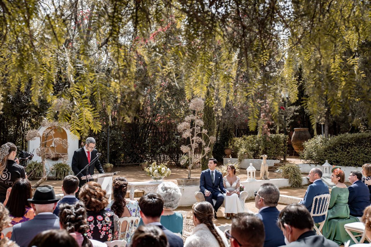 Ceremonia de boda civil al aire libre con los novios sentados en un sofá mirando a un chico durante una de las lecturas