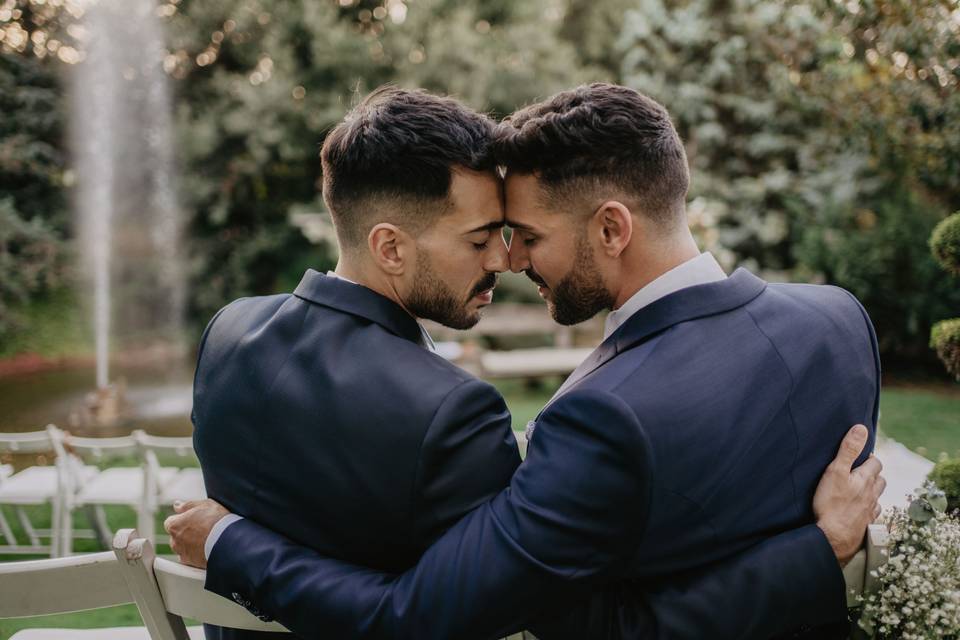 Dos chicos elegantemente vestidos con traje, con un peinado similar y barba, se abrazan